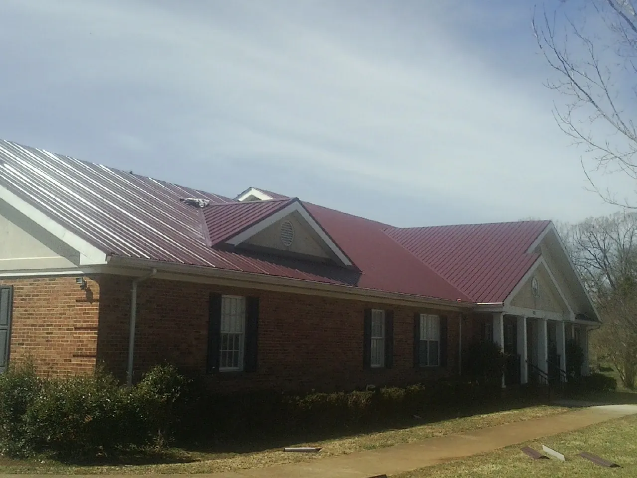 Red metal roof with gabled entries on a long brick building, from a Hail Damage Roof Repair job in Mount Union