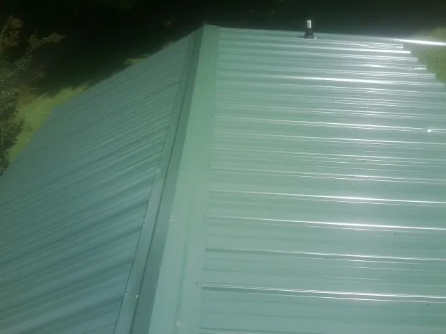 New green metal panels meeting at the ridge of a roof — Flat Roof Repair work by our crew in Mount Union